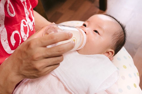 抱きかかえられ哺乳瓶からミルクを飲んでいる赤ちゃんの写真