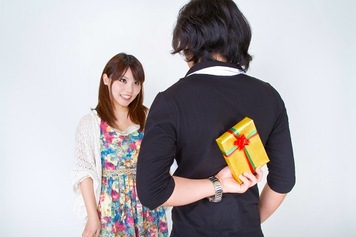 笑顔の女性と後ろ手にプレゼントを持つ男性が向かい合っている写真