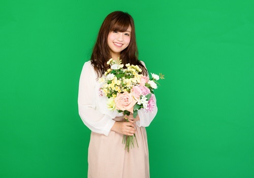 緑の背景に花束を抱えた笑顔の女性の写真
